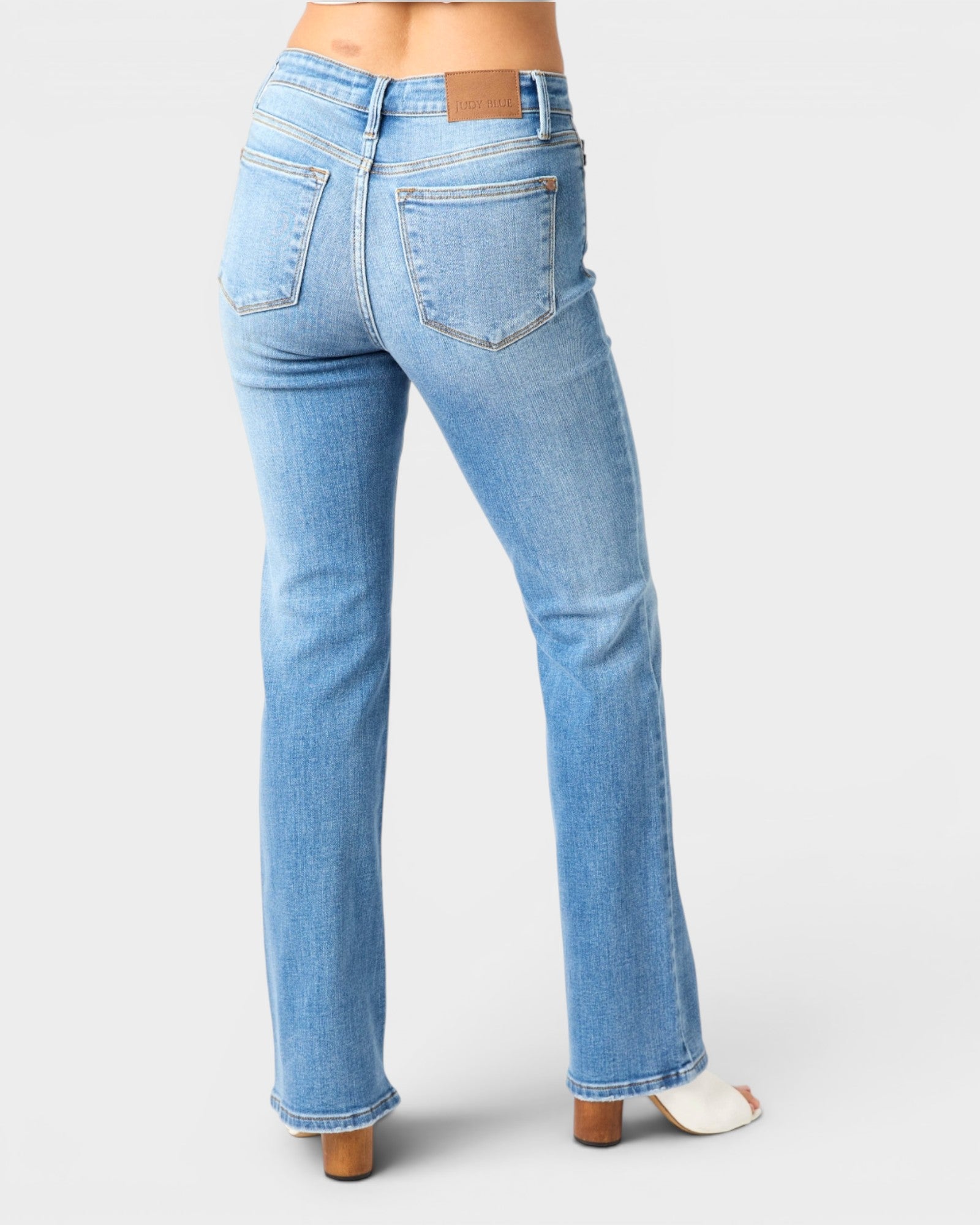 Rear view of a person wearing light blue denim jeans with a straight-to-flare leg, shown against a plain light gray studio background.