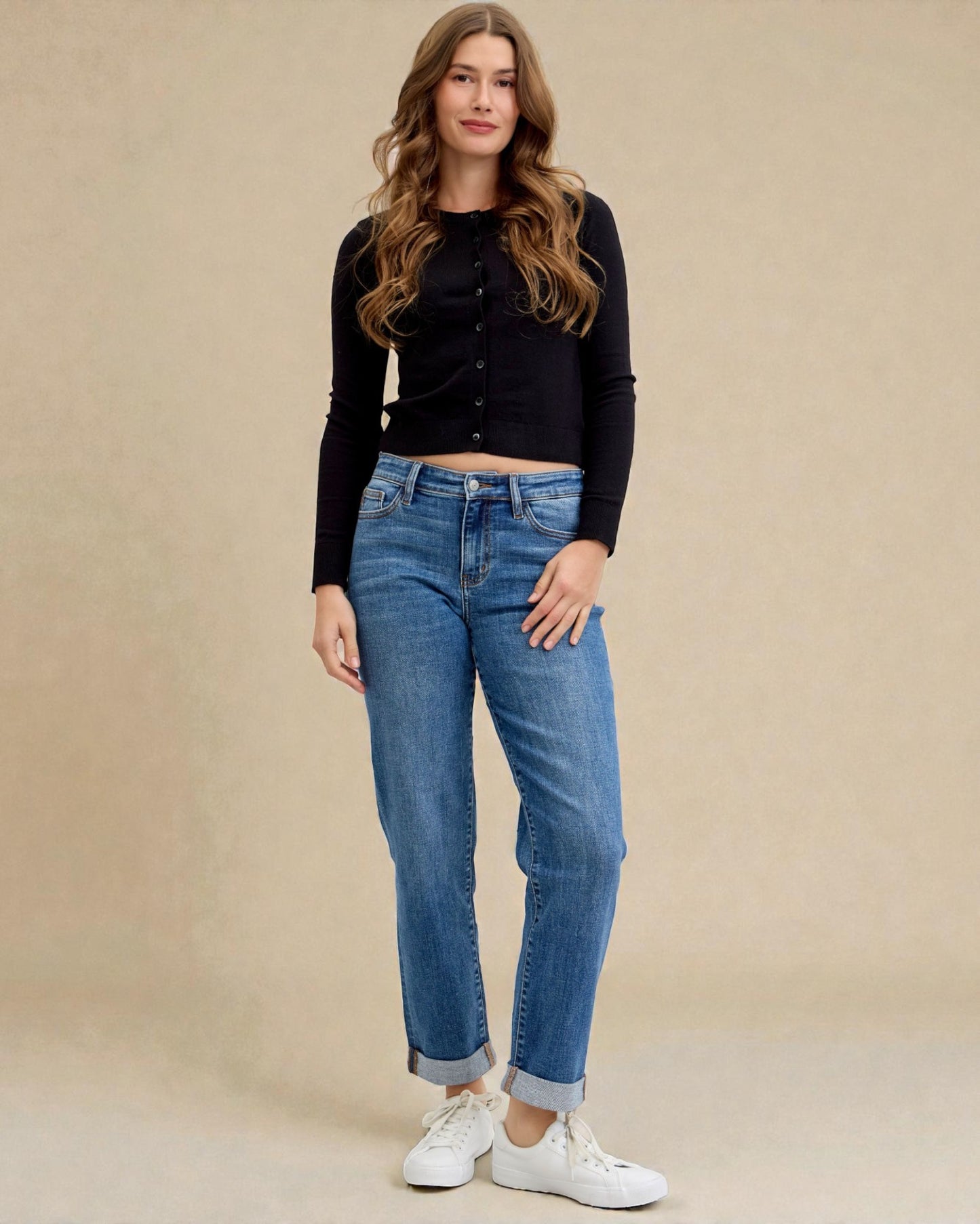 Woman wearing a black button-up shirt and blue jeans against a beige background