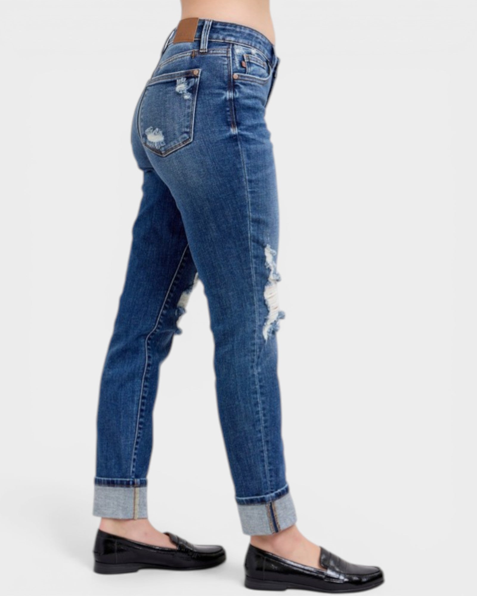 Blue jeans with distressed details worn by a person on a white background