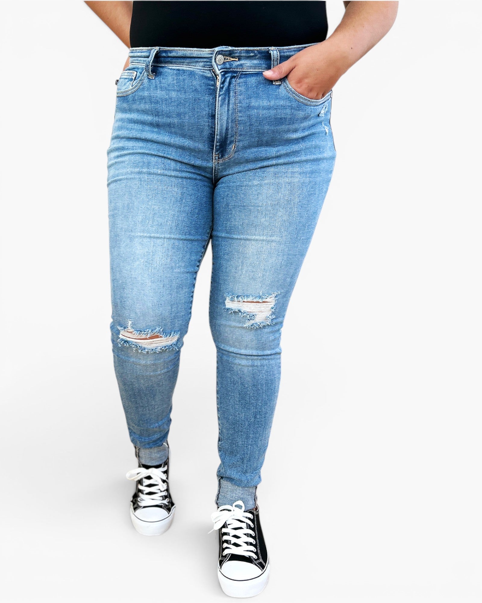 Light blue distressed skinny jeans worn by a model, paired with black and white sneakers, shown from the waist down on a light gray background.
