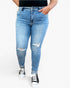 Light blue distressed skinny jeans worn by a model, paired with black and white sneakers, shown from the waist down on a light gray background.