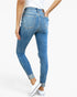 Rear three-quarter view of a person wearing blue skinny jeans with a white top and white sneakers against a light gray studio background.