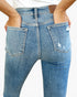 Close-up back view of a person wearing light blue denim jeans with a distressed rips detail on the right back pocket and a brown leather waistband patch.