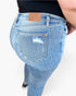 Close-up back view of a person wearing light blue distressed skinny jeans with a tan leather brand patch on the waistband, photographed against a plain light background.