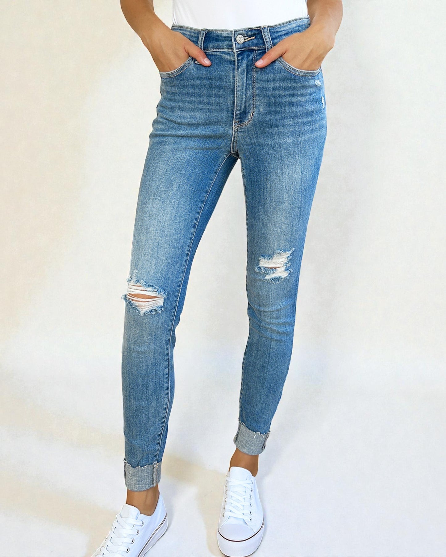 Person wearing distressed blue jeans with a white background