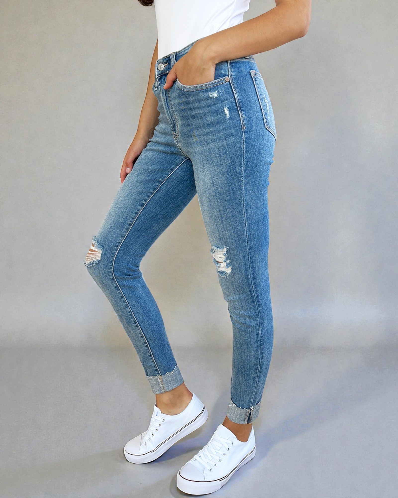 Person wearing blue jeans and white sneakers on a plain background