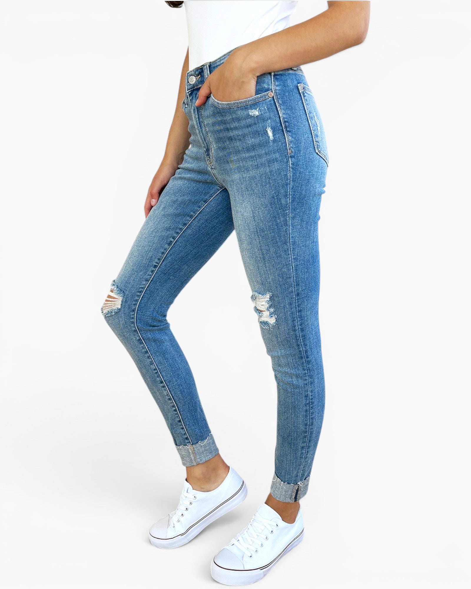 A person wearing light blue high-waisted skinny jeans with distressed details and cuffed hems, paired with white sneakers, shown against a plain white studio background.