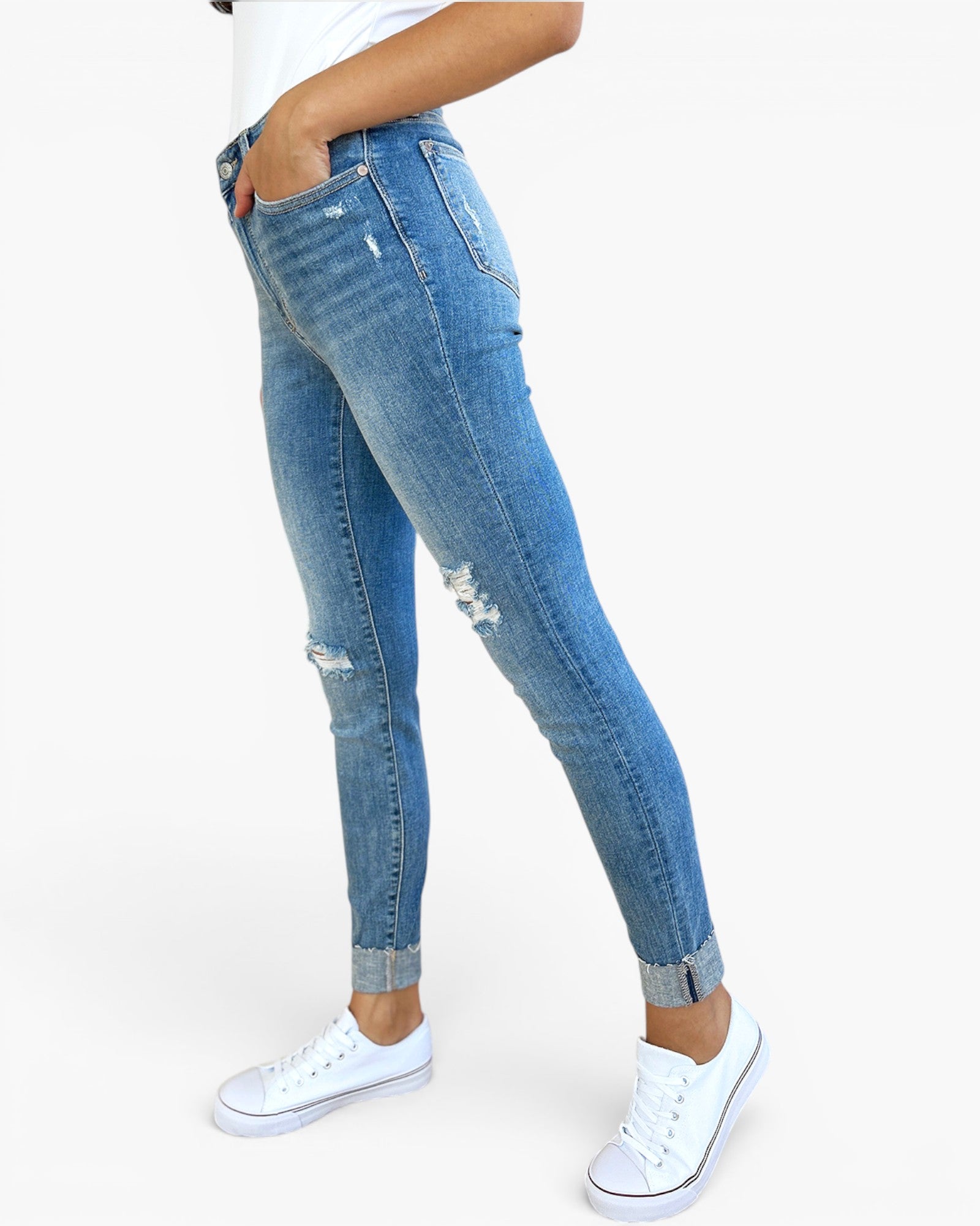 A person wearing light blue distressed skinny jeans with cuffed hems and white low-top sneakers, shown from the waist down against a plain light gray studio background.