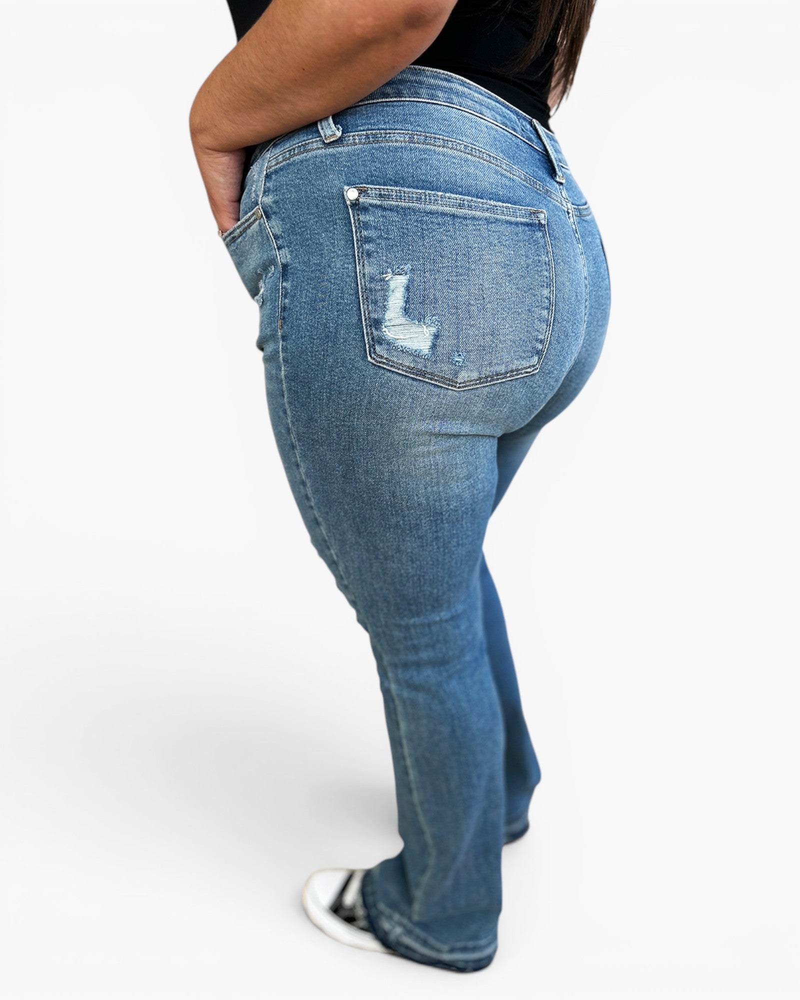 A person wearing medium-wash blue denim jeans with a distressed back pocket detail, shown from a side-rear angle against a plain light background.
