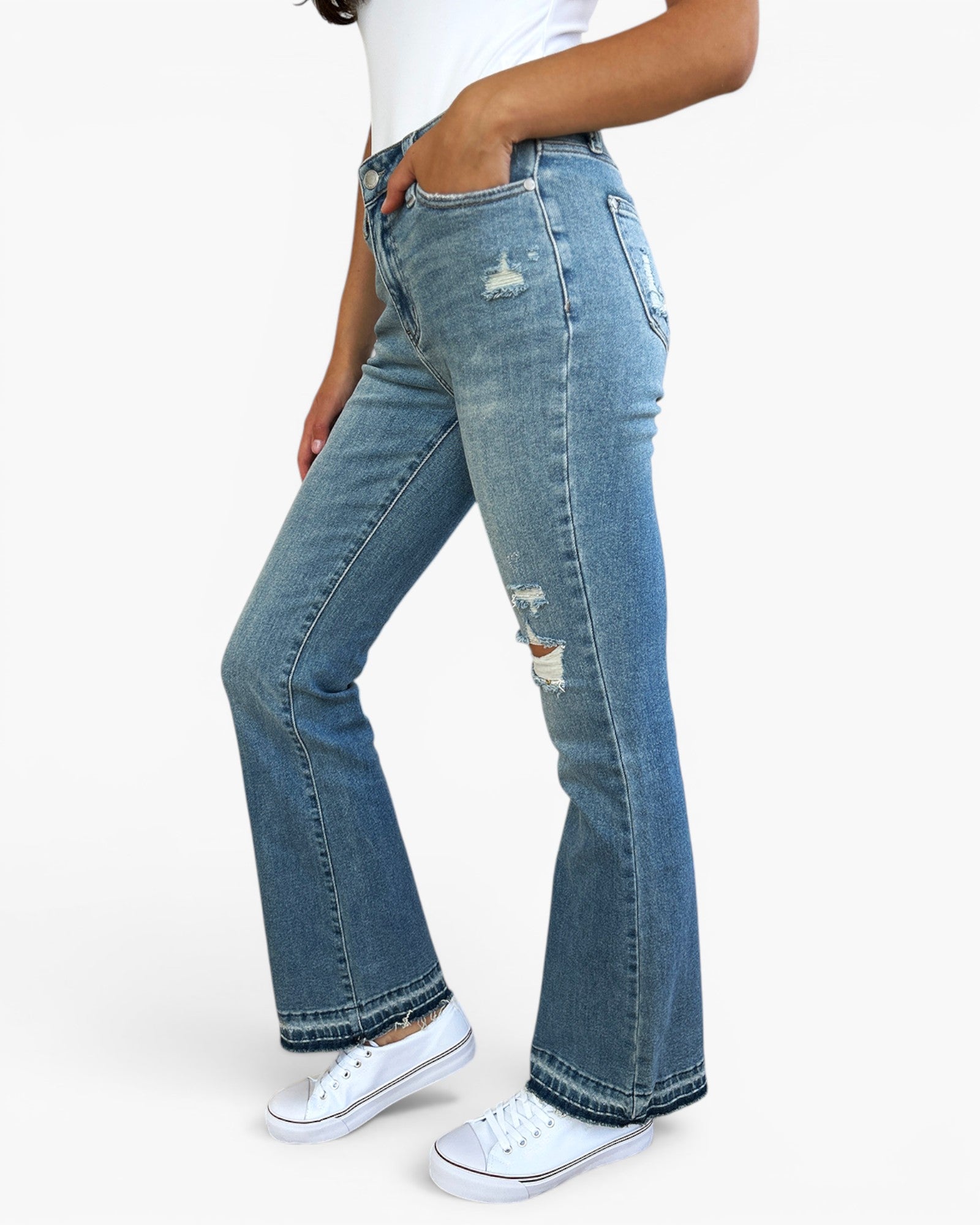 A person wearing light blue high-waisted flare jeans with distressed details and white sneakers, shown from the waist down against a plain light background.