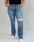 Person wearing blue jeans with a distressed design on a plain background