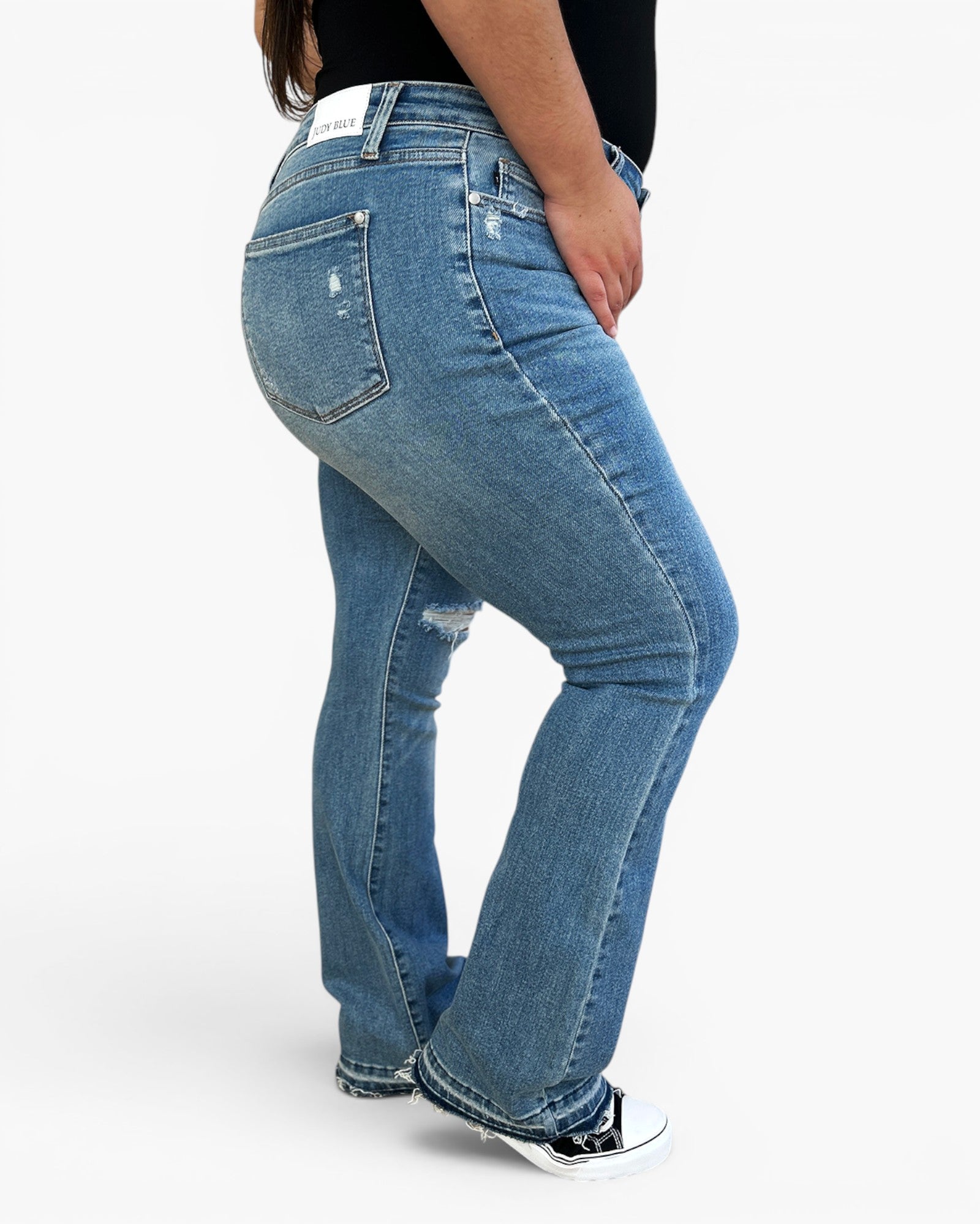 A person wearing medium-wash blue denim flare jeans with distressed details, shown from a side-back angle against a plain white studio background.