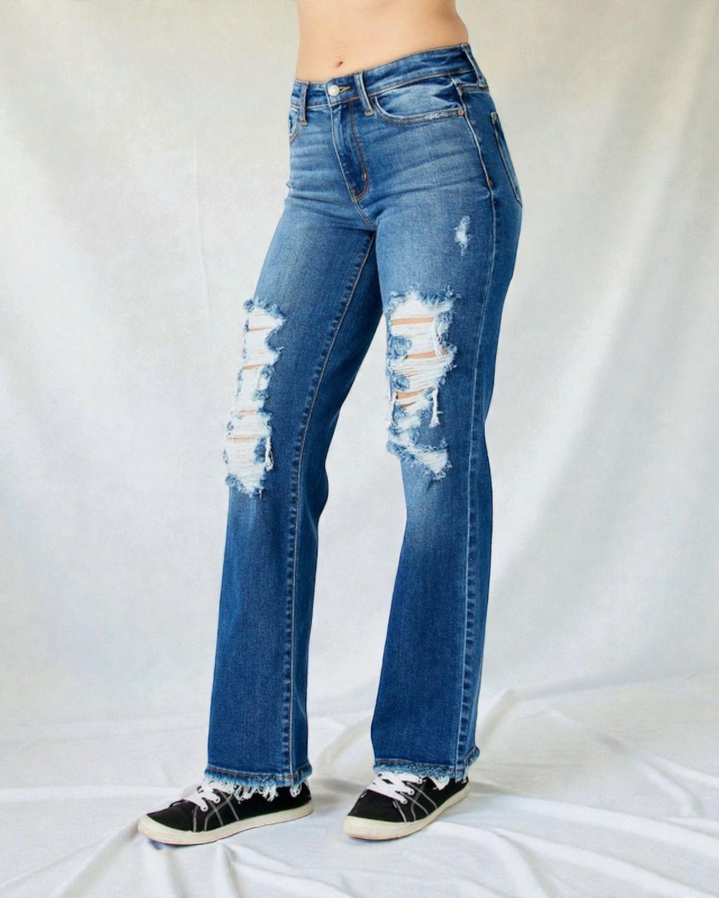 Distressed blue jeans worn by a person on a white background
