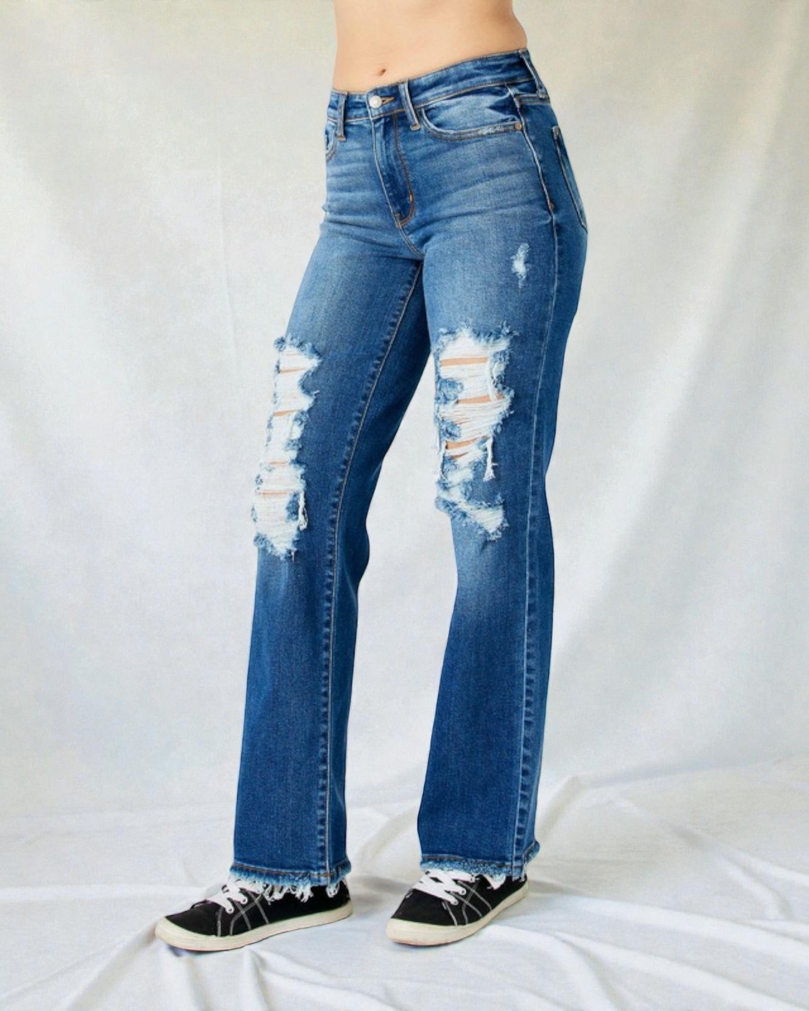 Distressed blue jeans worn by a person on a white background