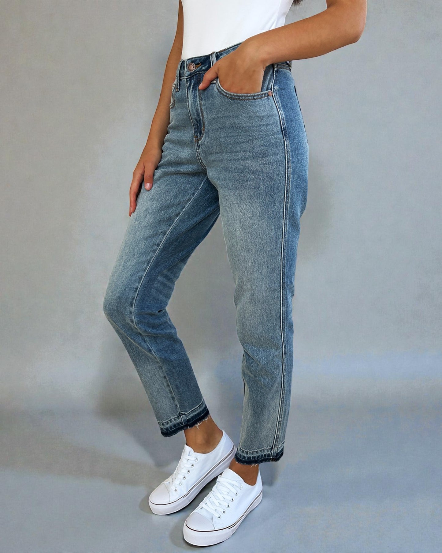 Person wearing blue jeans and white sneakers on a plain background