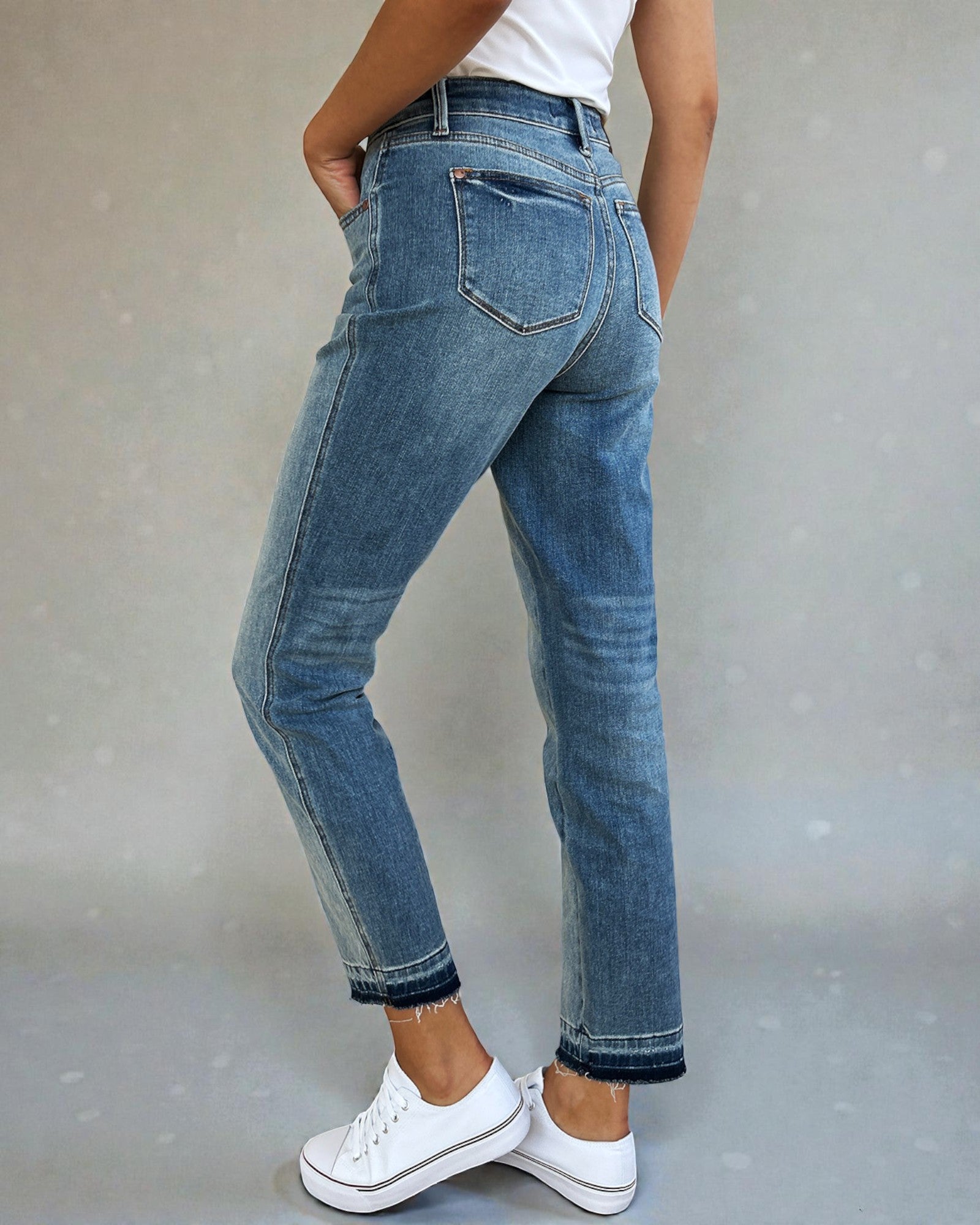 Person wearing blue jeans and white sneakers on a plain background