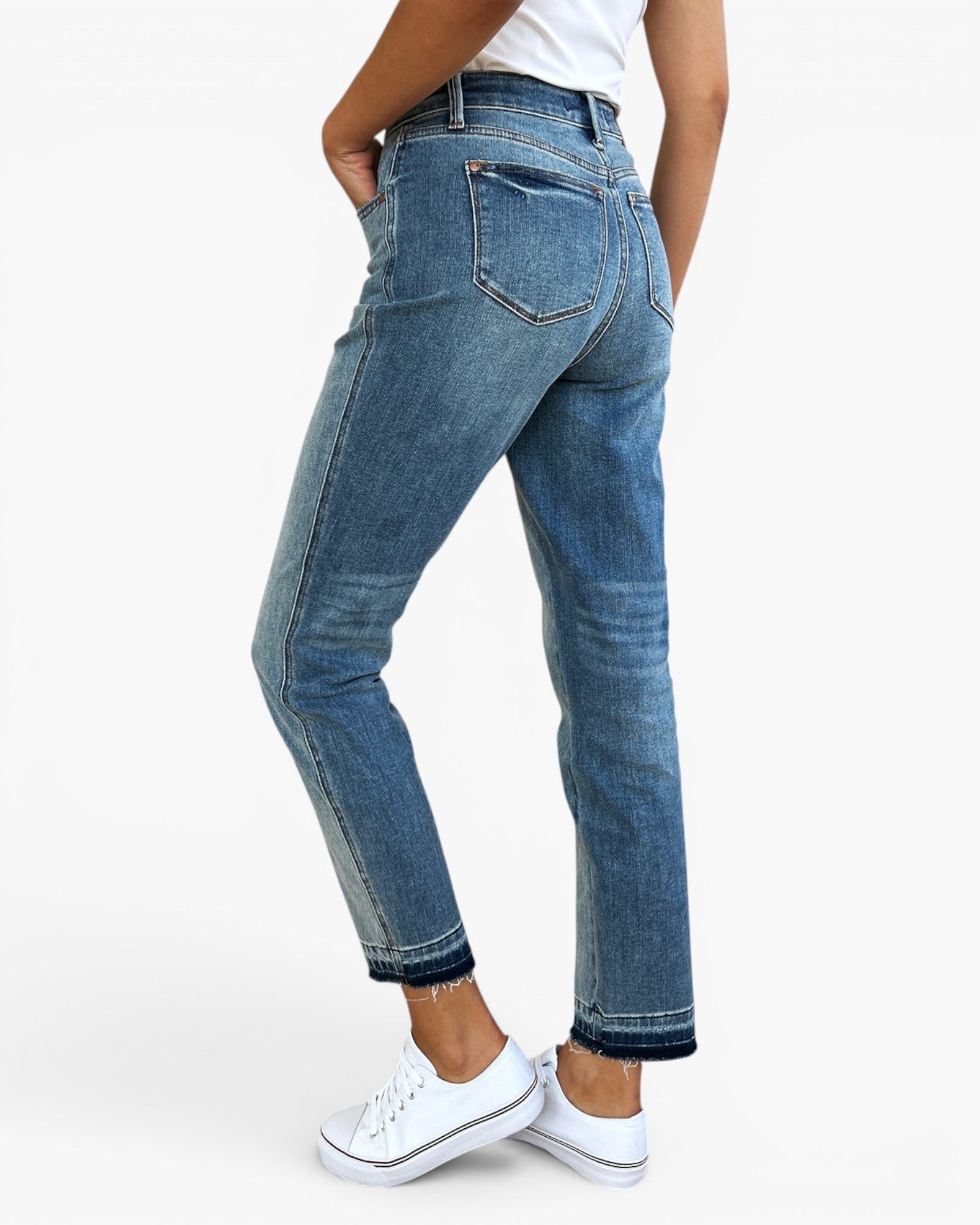 A person wearing blue denim jeans with a straight-to-ripped leg, shown from the back and side against a clean white studio background. The model is also wearing a white top and white sneakers.