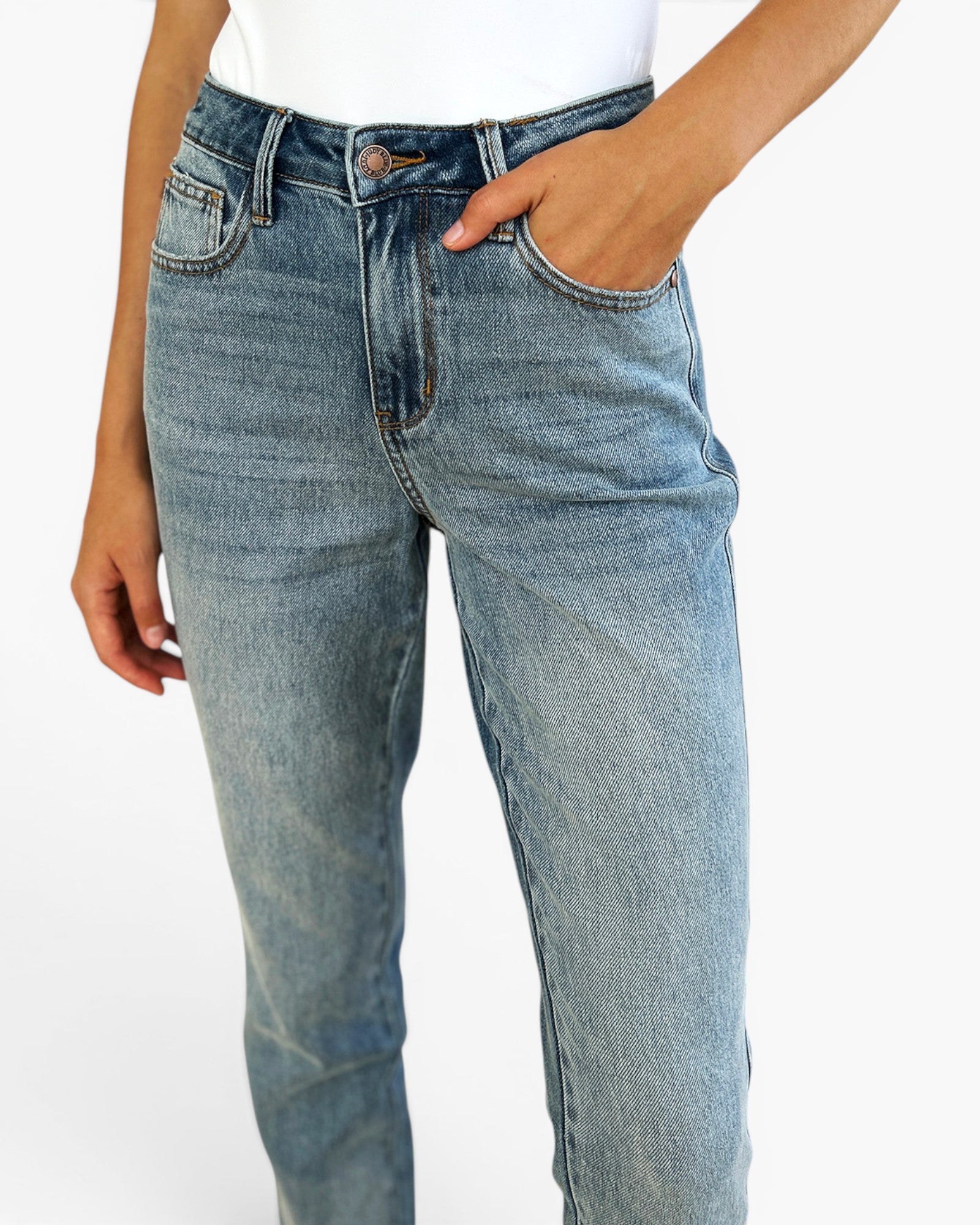 A close-up of a person wearing light-wash blue denim jeans with a white top, shown from the waist down against a plain white background.
