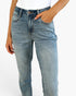 A close-up of a person wearing light-wash blue denim jeans with a white top, shown from the waist down against a plain white background.