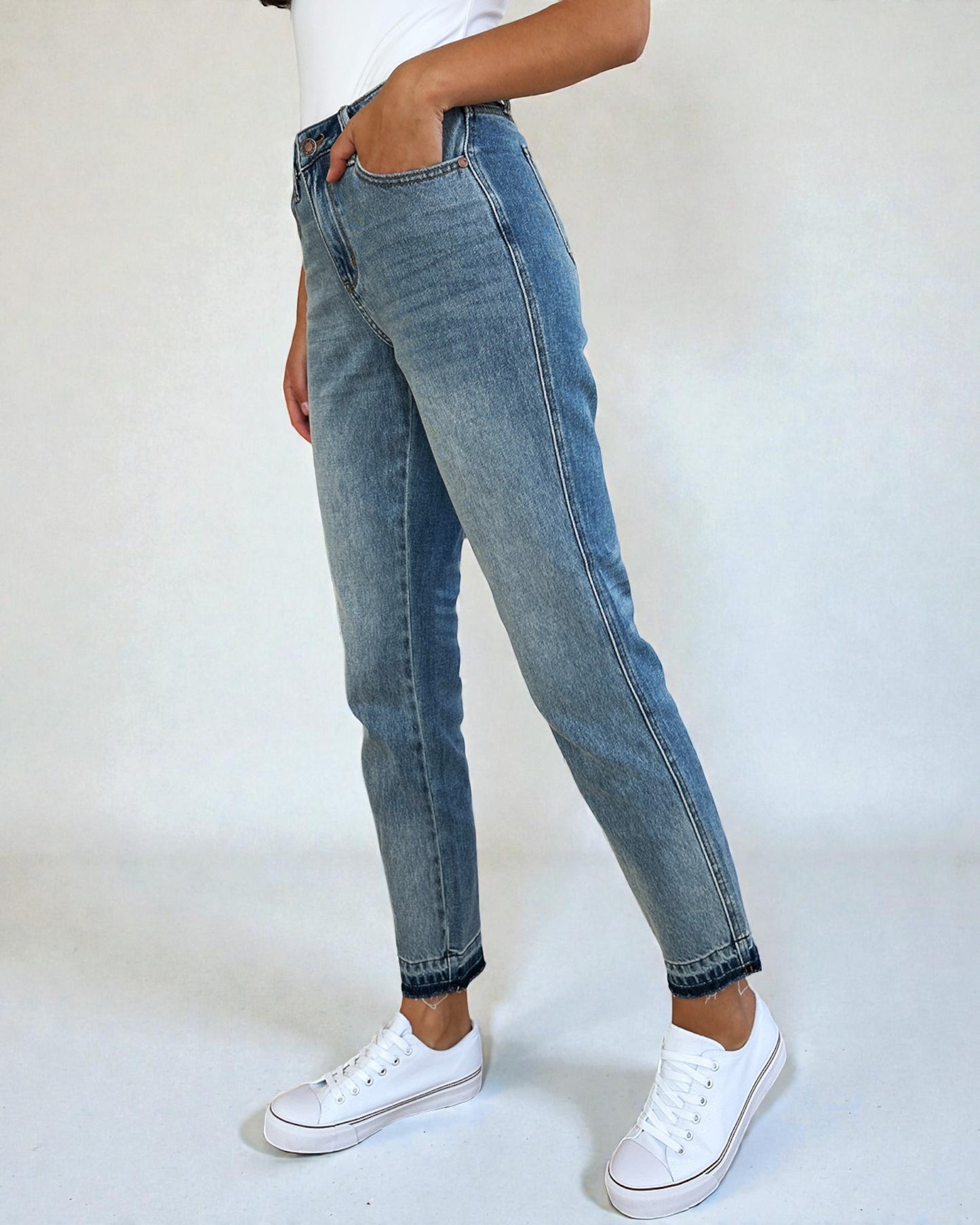 Person wearing light blue jeans and white sneakers on a plain background