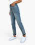 A person wearing medium-wash blue denim jeans with rolled cuffs and white low-top sneakers, shown from the waist down against a clean white studio background.