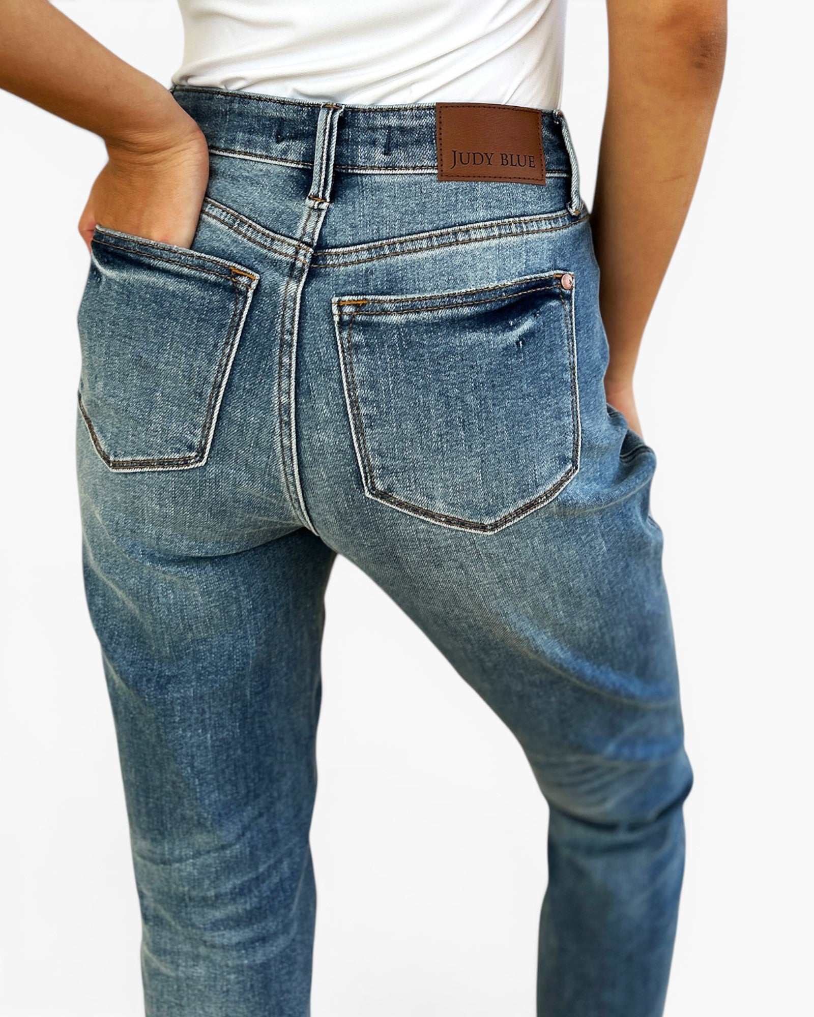 Rear view of a person wearing blue denim jeans with a brown leather patch on the back waistband that reads 'JUDY BUEY'.