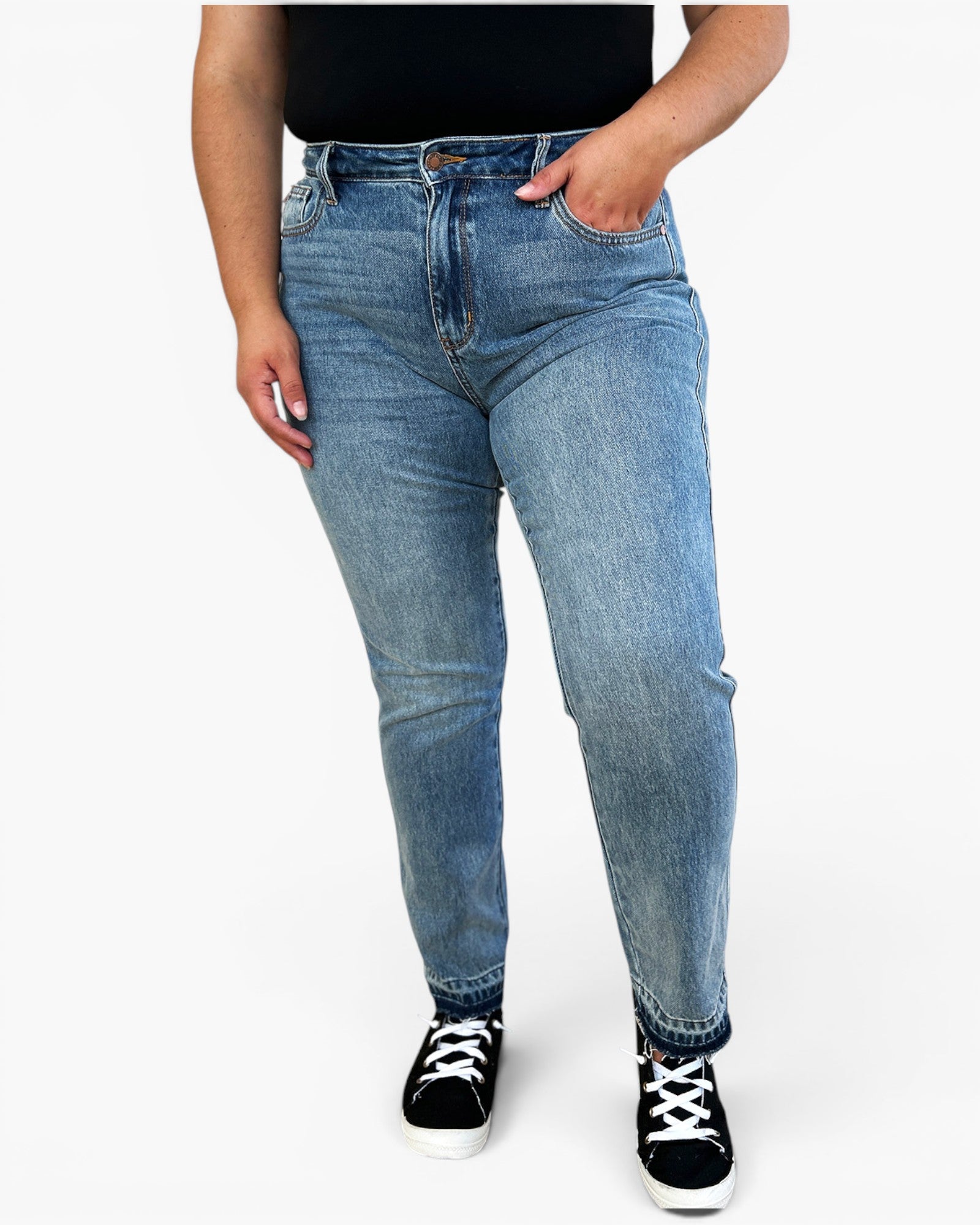 A person wearing light blue slim-fit denim jeans with a black top and black low-top sneakers, shown from the waist down against a plain white studio background.