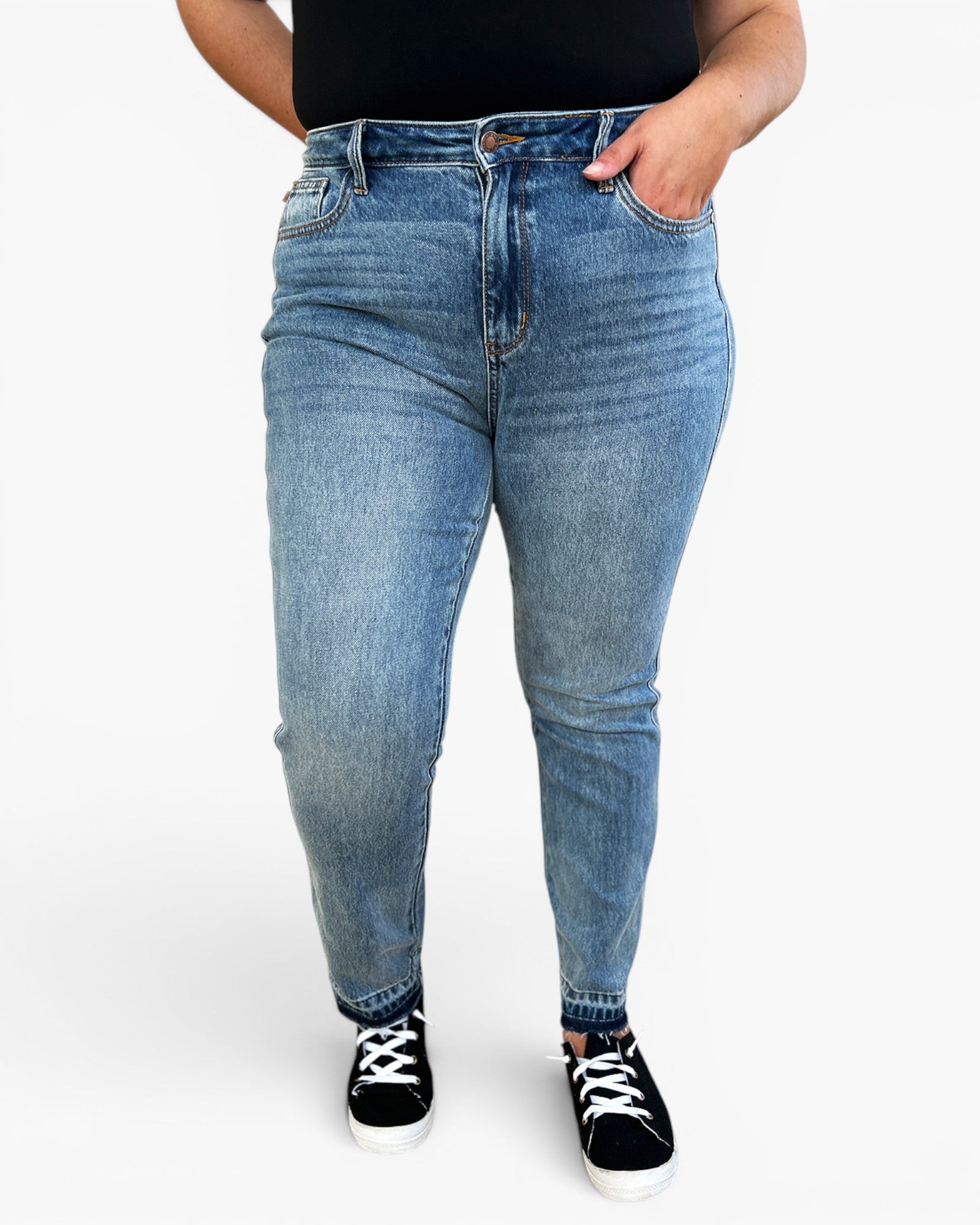 A person wearing light blue high-waisted skinny jeans, a black top, and black canvas sneakers with white laces, standing against a plain white studio background.