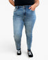 A person wearing light blue high-waisted skinny jeans, a black top, and black canvas sneakers with white laces, standing against a plain white studio background.