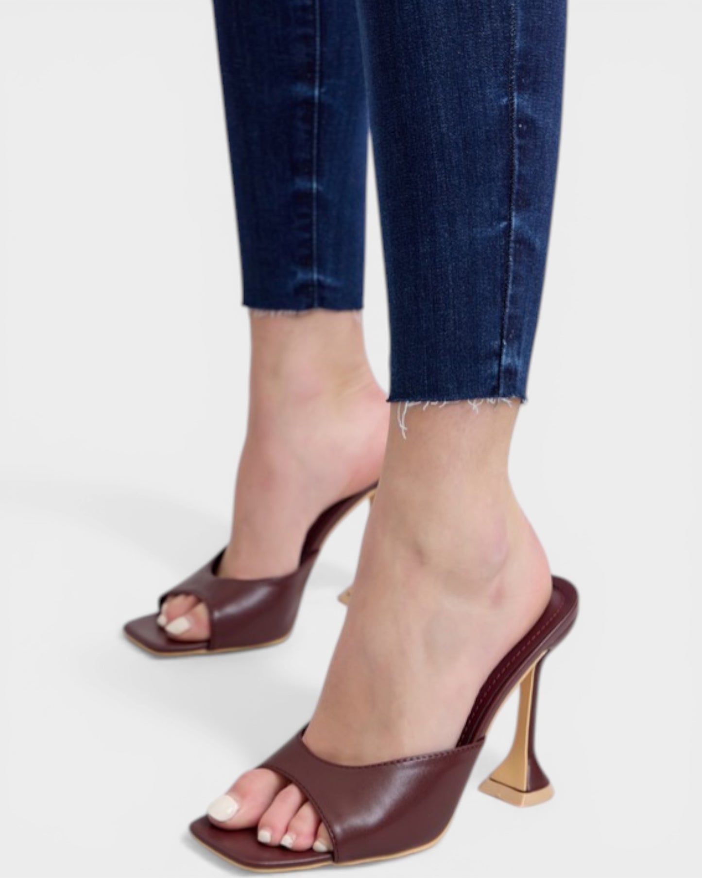 Brown high-heeled sandals worn with blue jeans on a white background