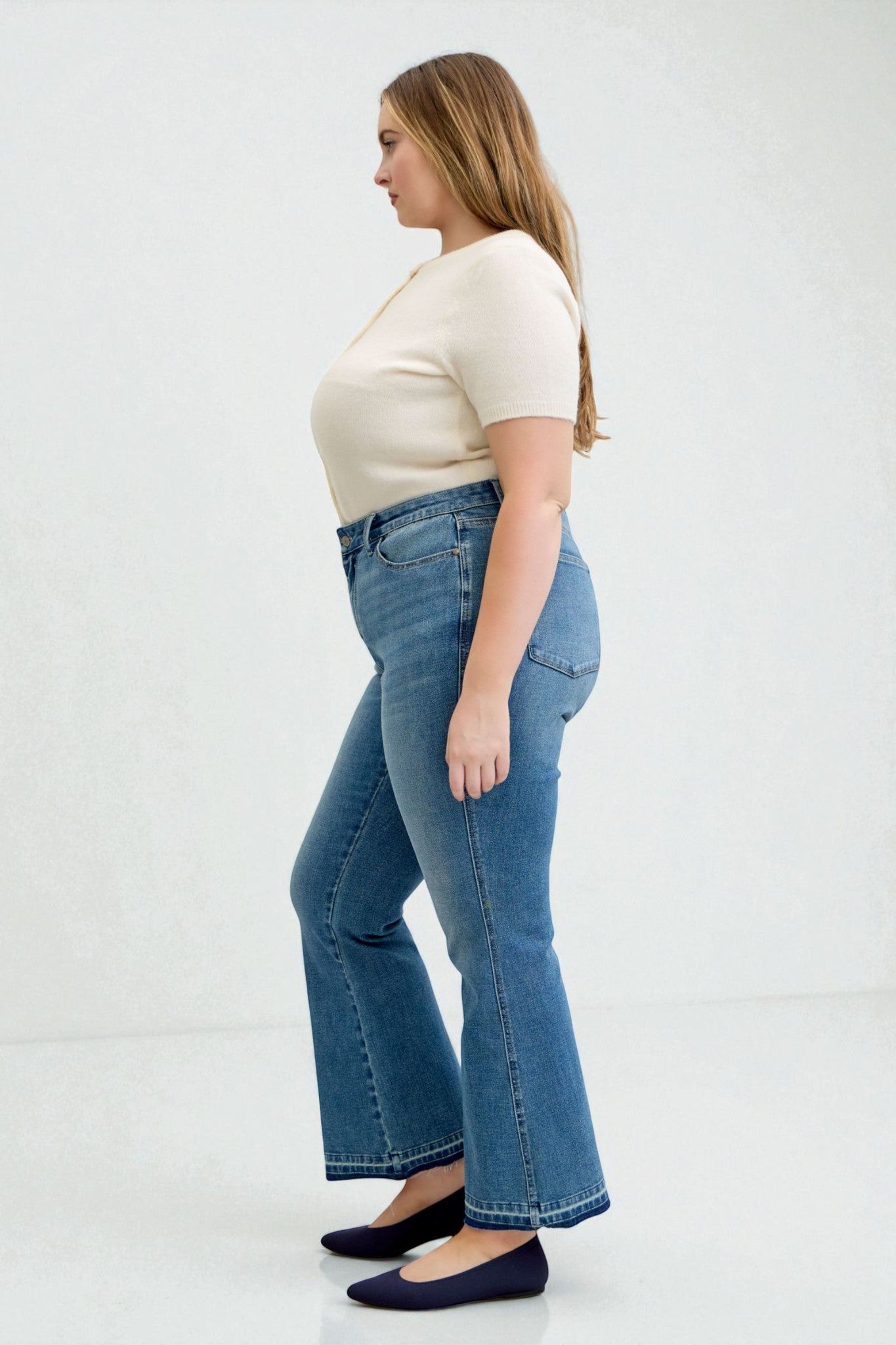 Woman wearing blue jeans and a cream top on a white background