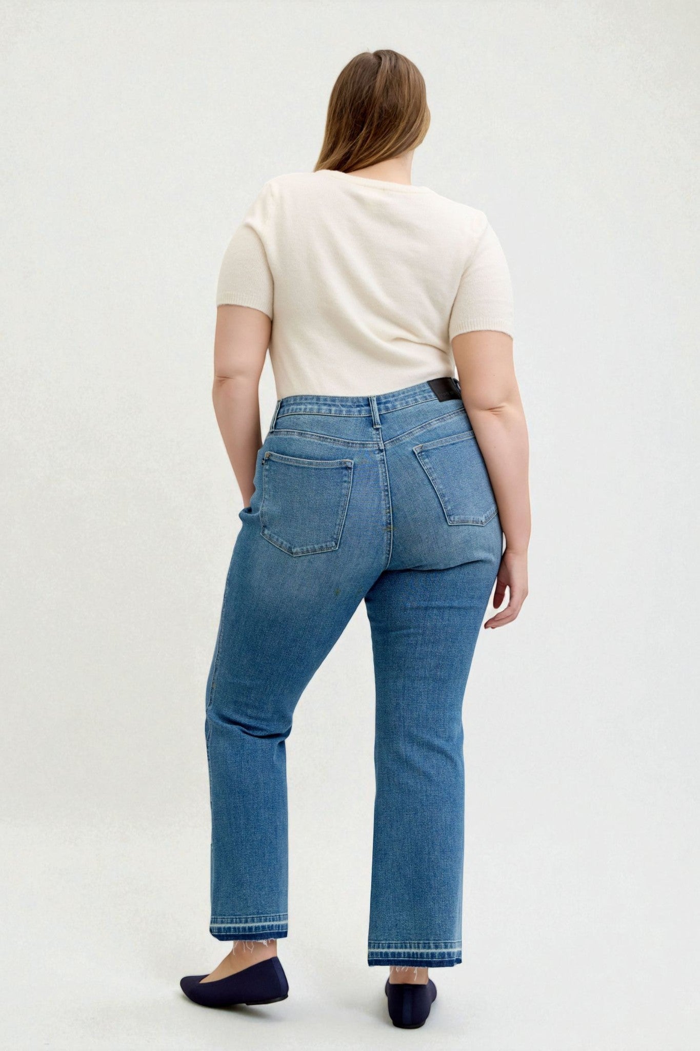 Person wearing blue jeans and a white top on a plain background