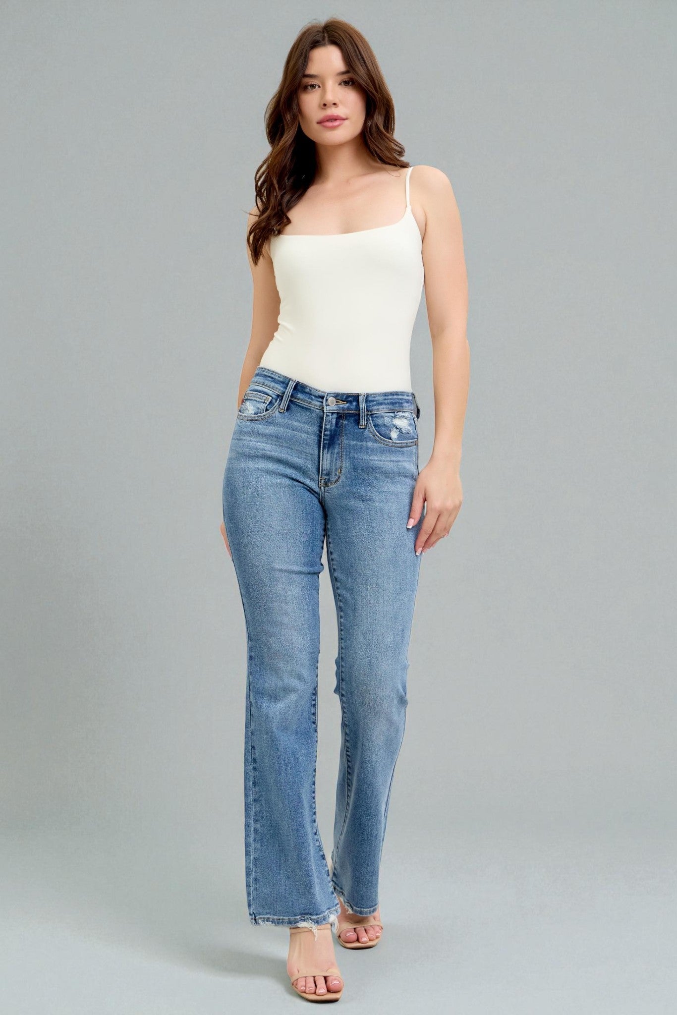 Woman wearing a white top and blue jeans on a gray background