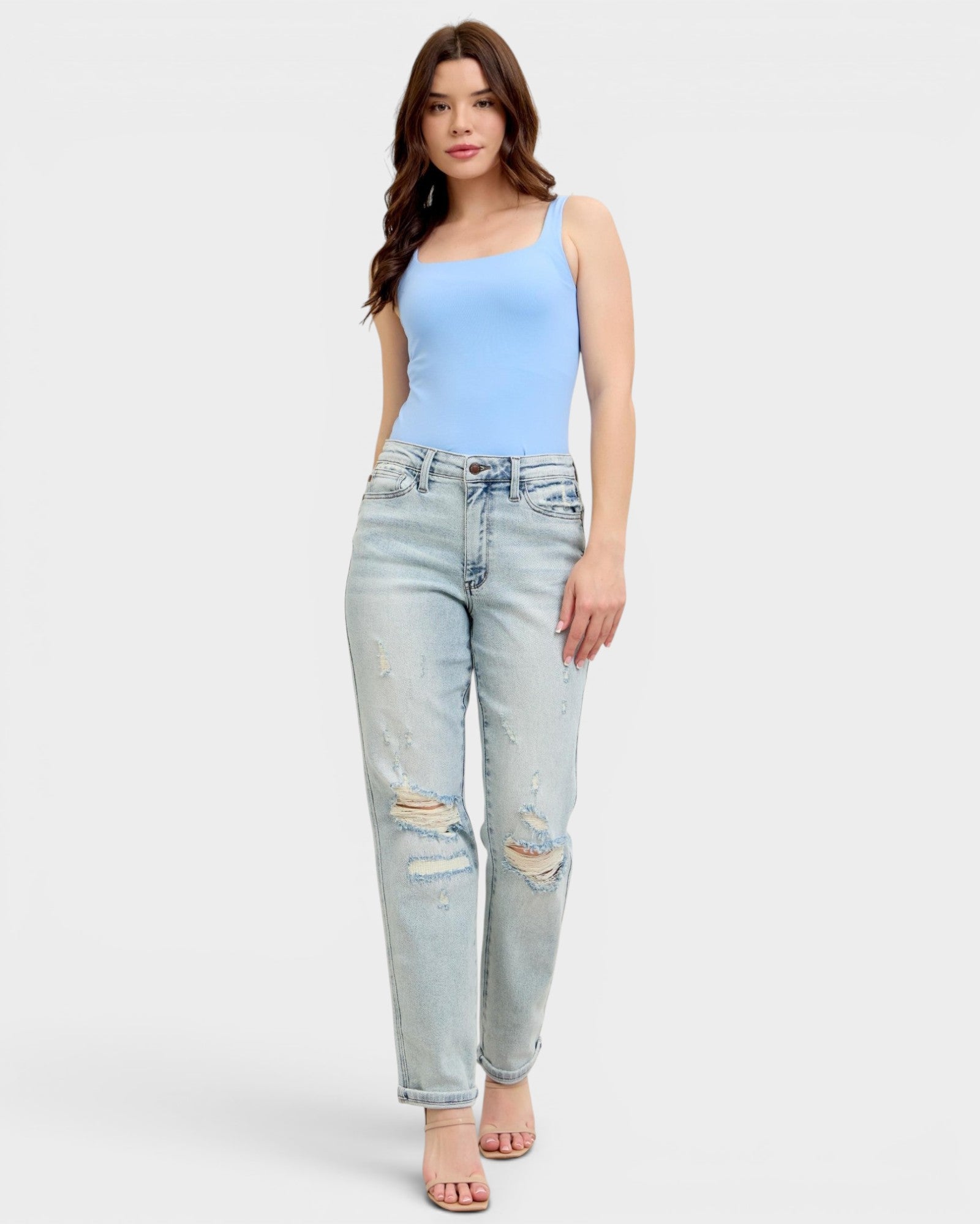 Woman wearing a light blue sleeveless top and distressed light blue jeans on a white background