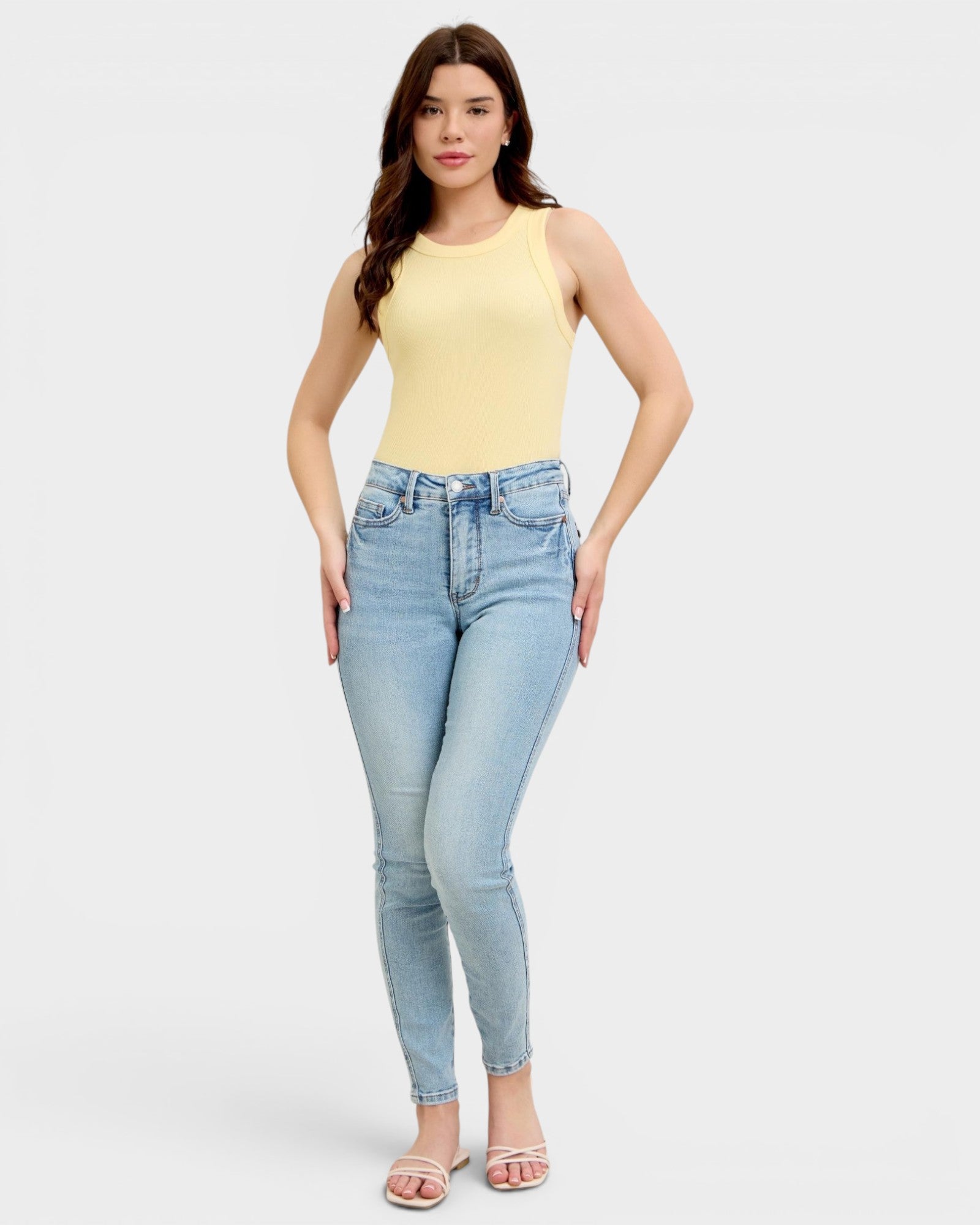 Woman wearing a yellow sleeveless top and light blue jeans on a white background