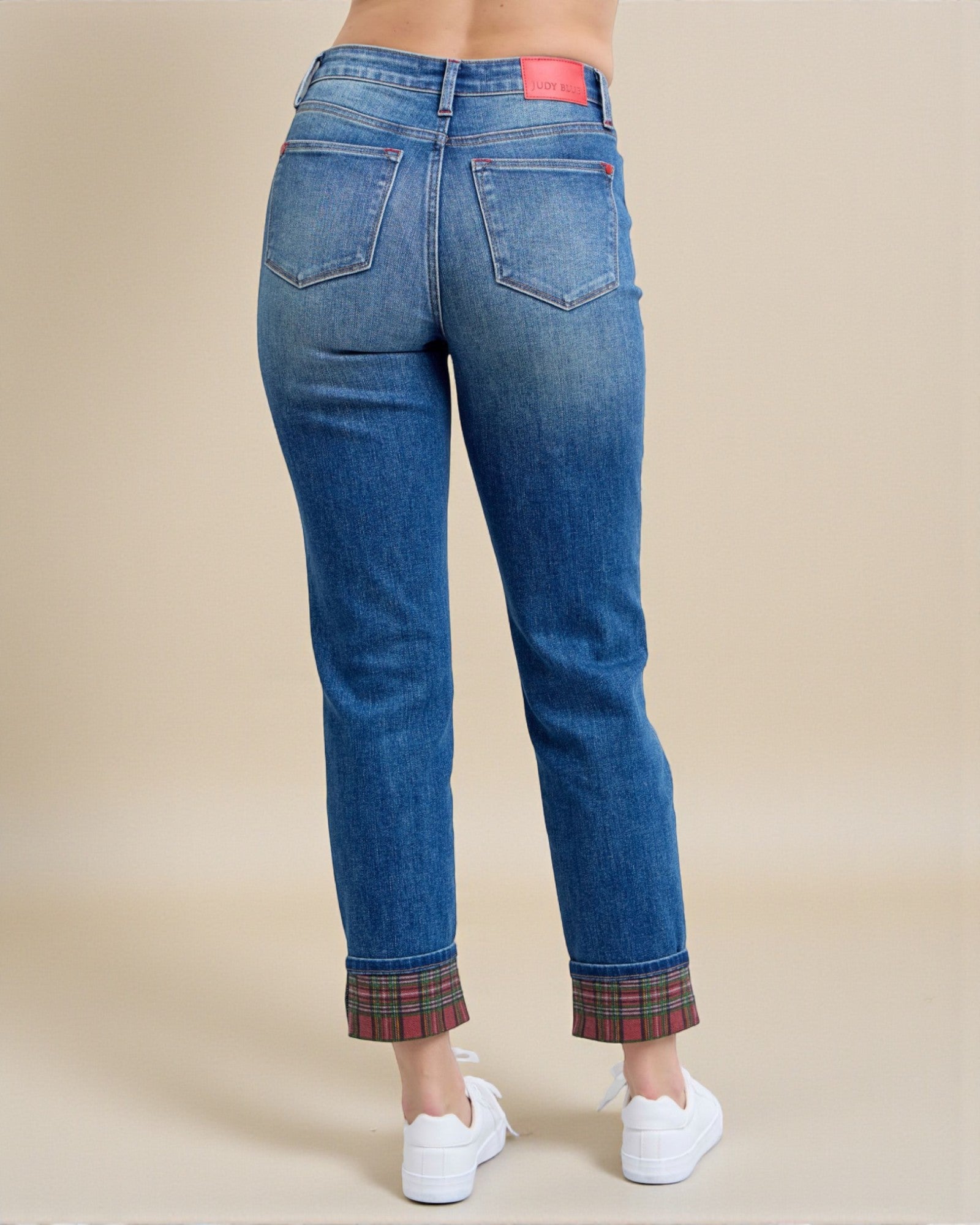 Blue jeans with plaid cuffs worn by a person on a beige background