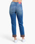 Back view of a person wearing blue denim jeans with rolled cuffs showing a plaid lining, paired with white sneakers, on a light gray studio background.