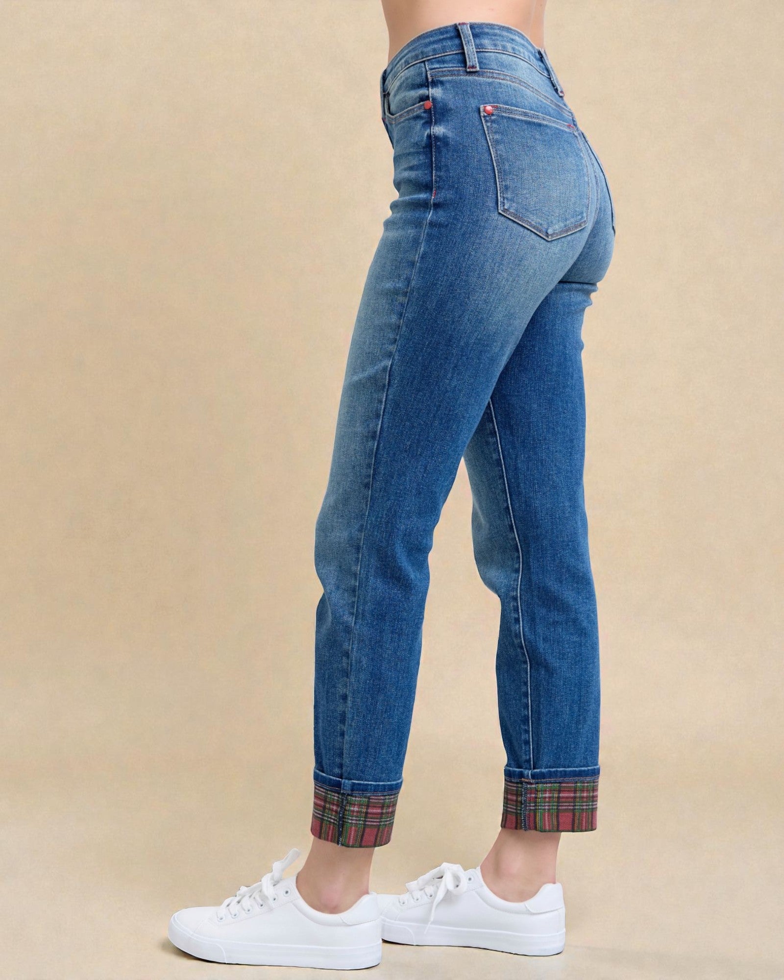 Blue jeans with plaid cuffs worn by a person on a beige background