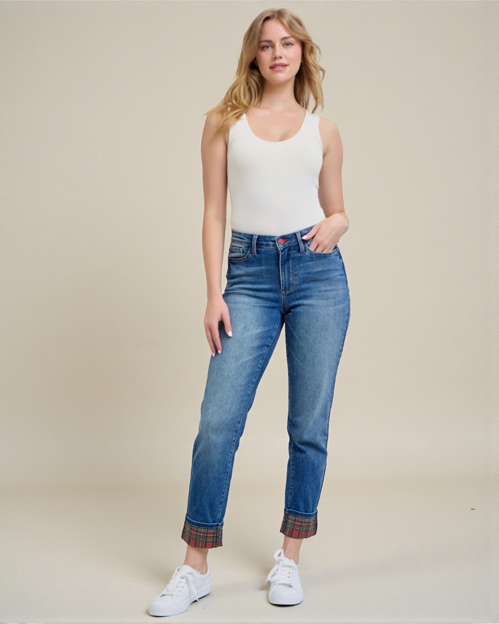 Woman wearing blue jeans and a white tank top on a beige background