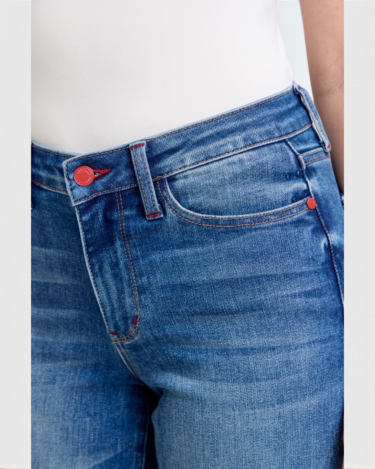 Close-up of blue jeans with a red button and zipper on a white background