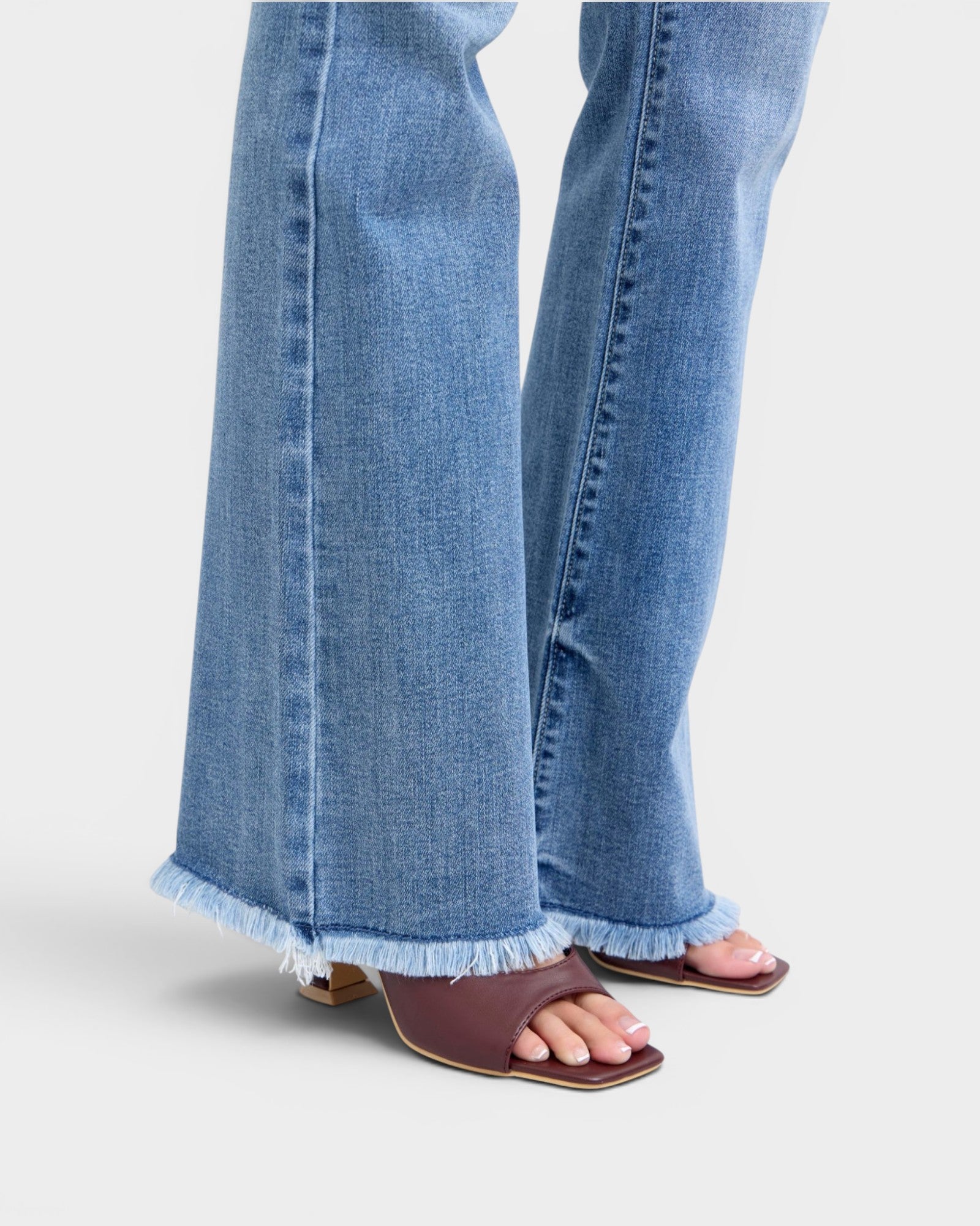 Denim pants with ruffled hem and brown sandals on a light gray background
