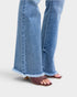 Denim pants with ruffled hem and brown sandals on a light gray background