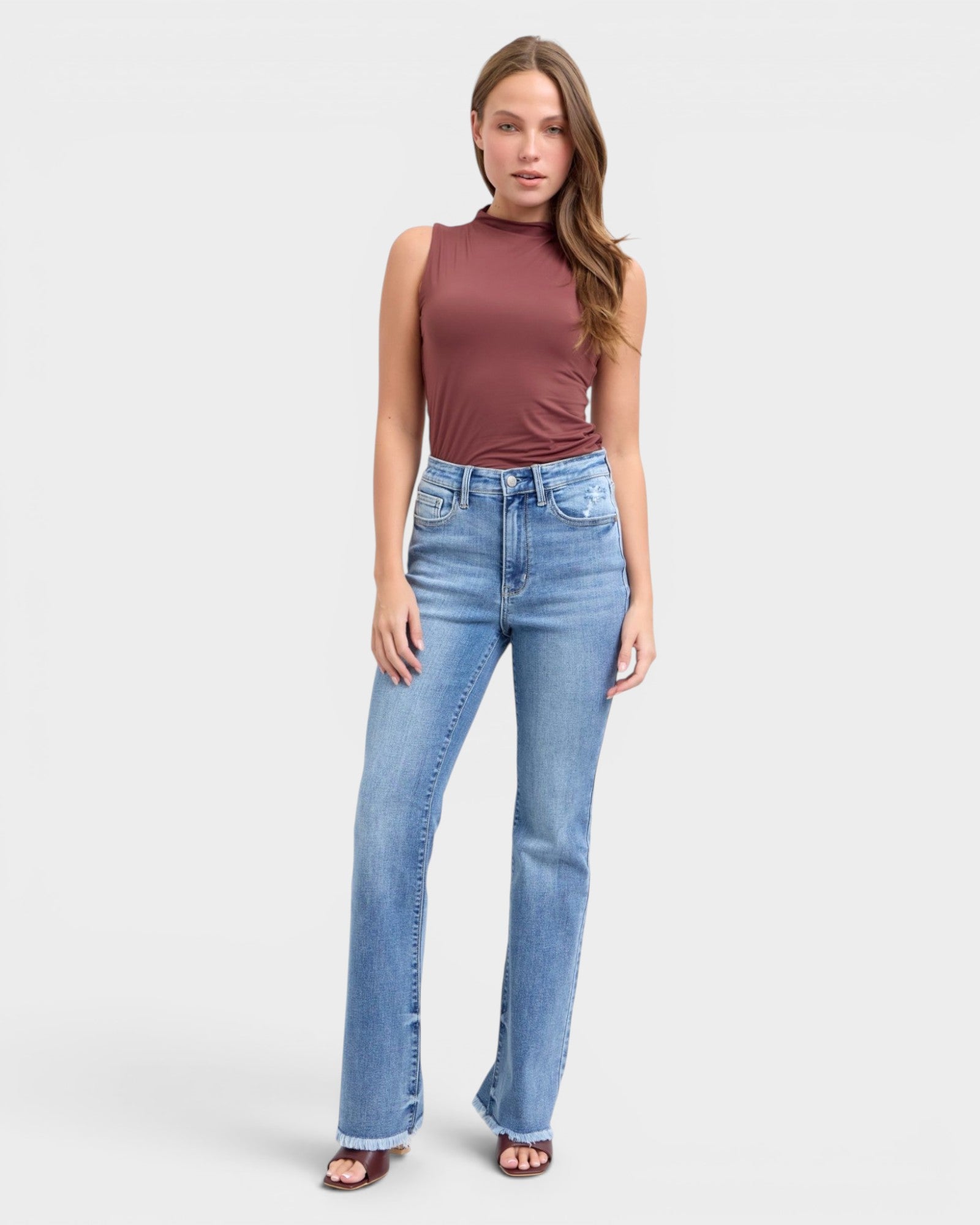 Woman wearing a sleeveless brown top and light blue jeans on a white background