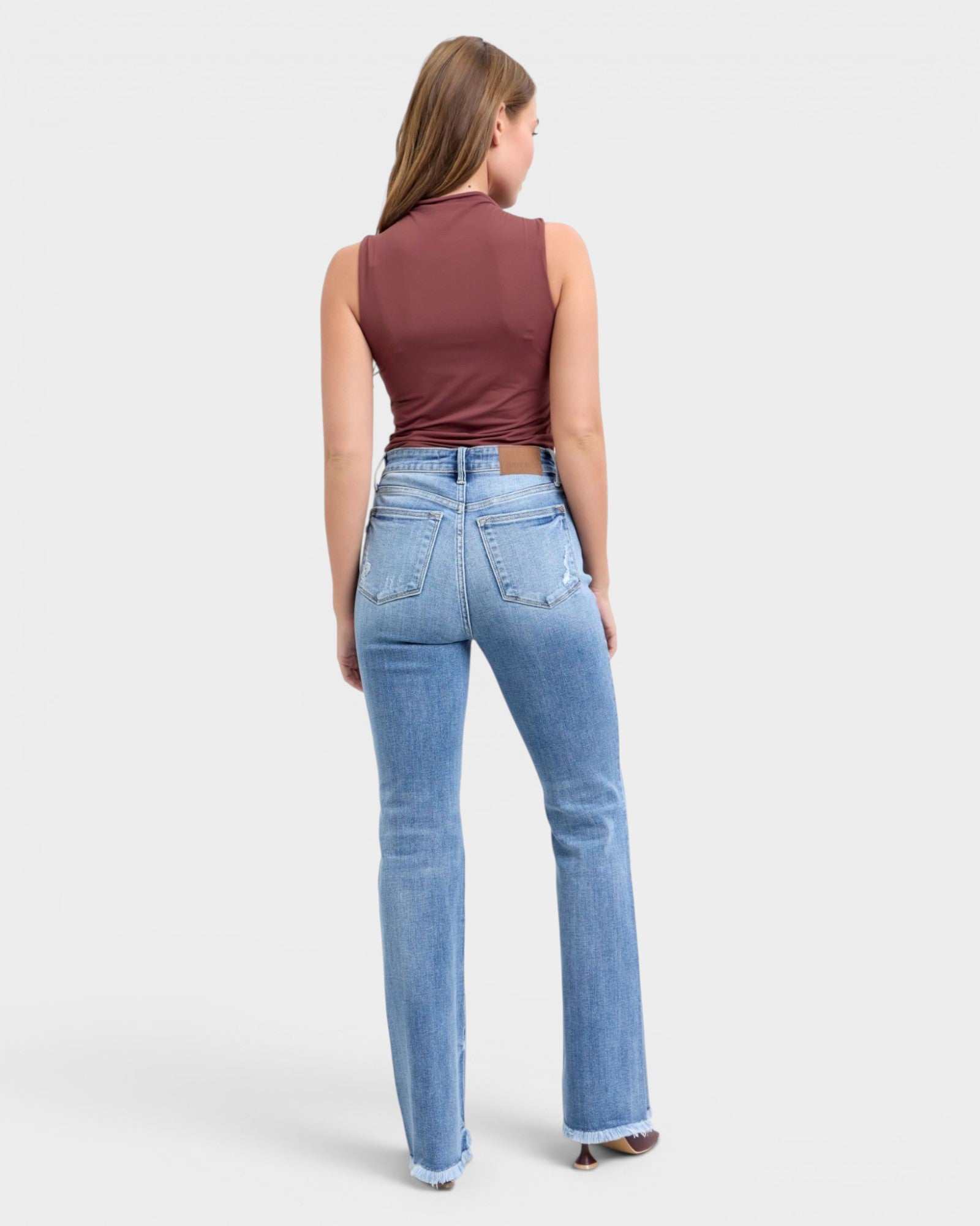 Woman wearing blue jeans and a maroon top on a light gray background