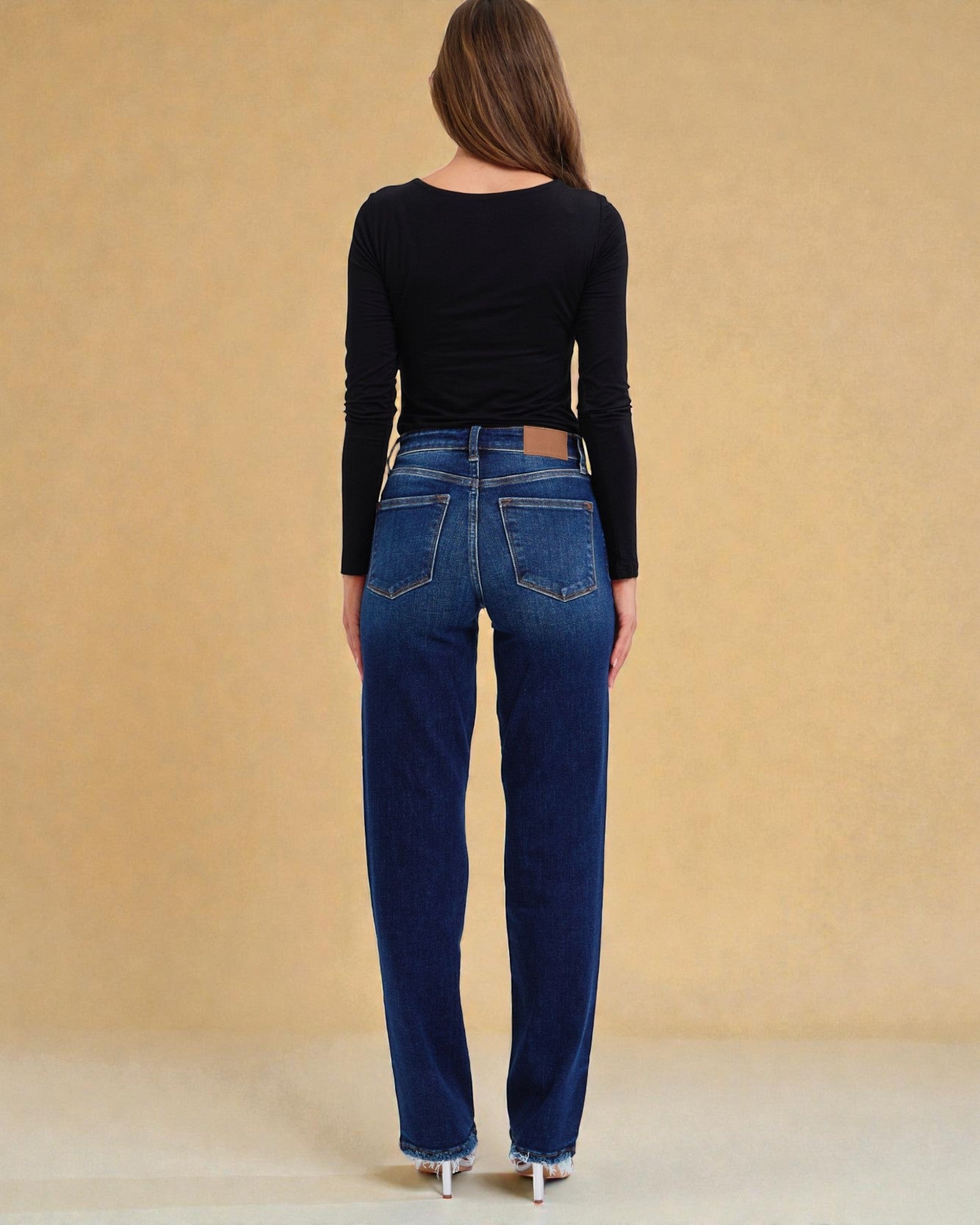 Person wearing blue jeans and a black long-sleeve top against a beige background