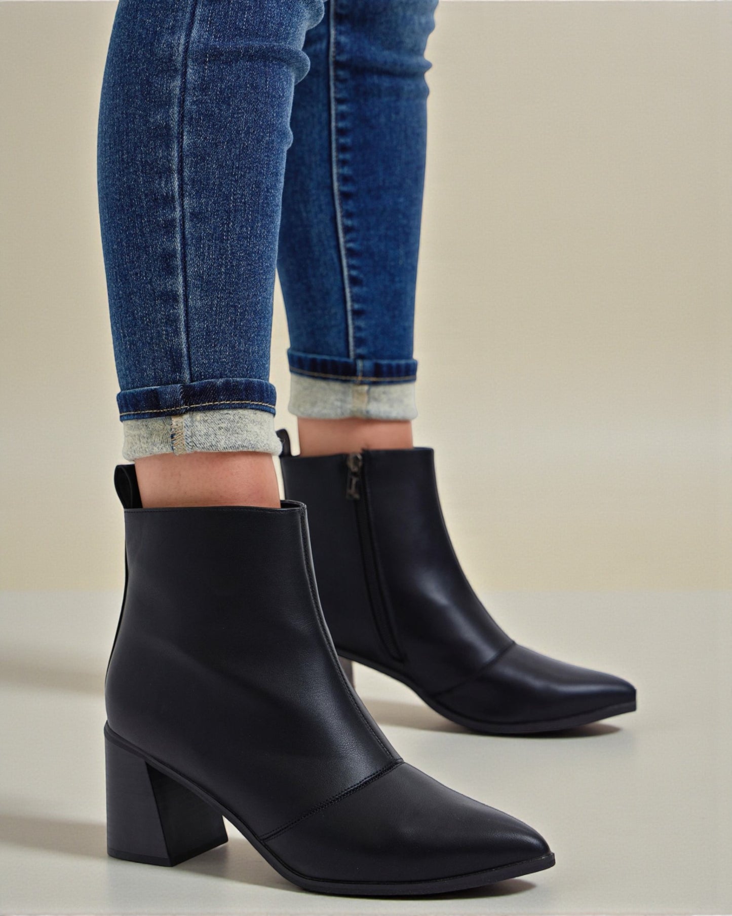Black ankle boots worn with blue jeans on a neutral background