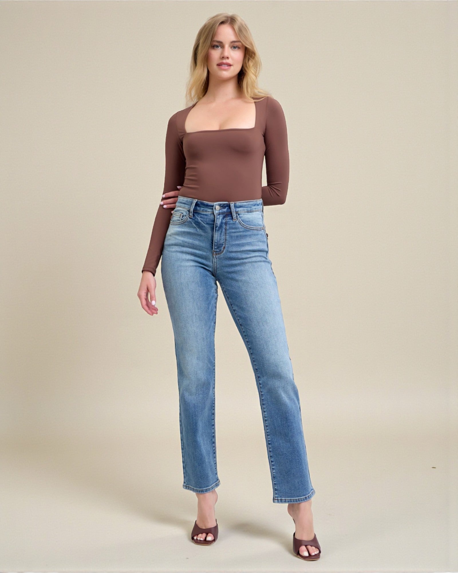 Woman wearing a brown long-sleeve top and blue jeans on a beige background