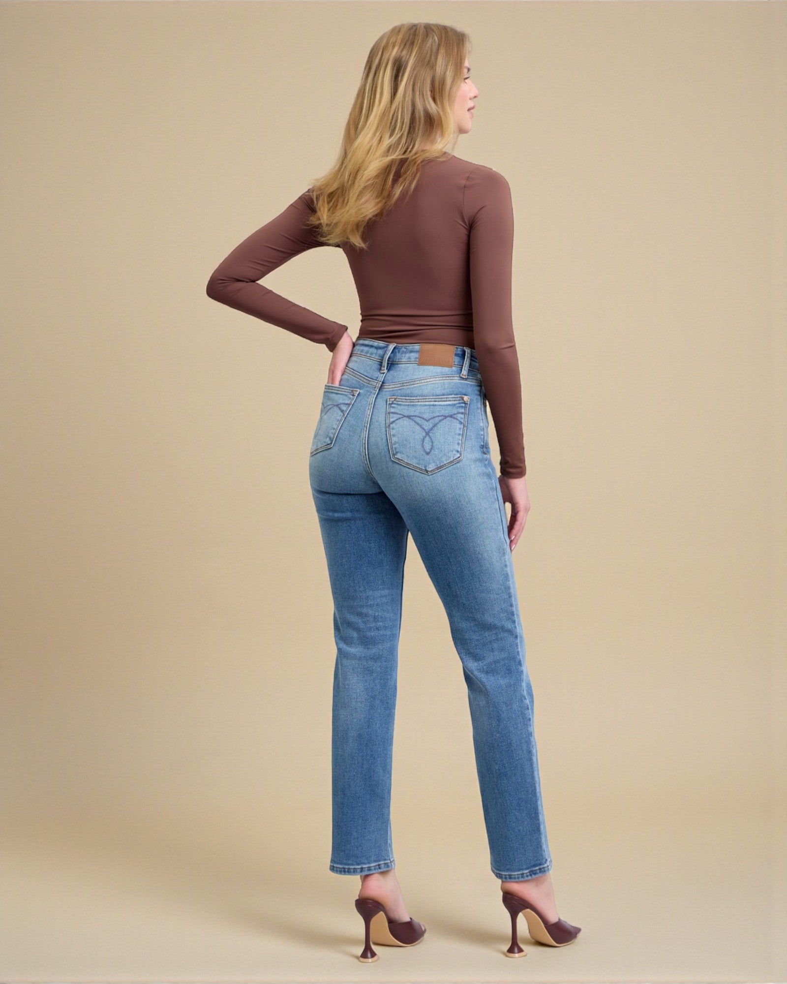 Woman wearing blue jeans and a brown top on a beige background