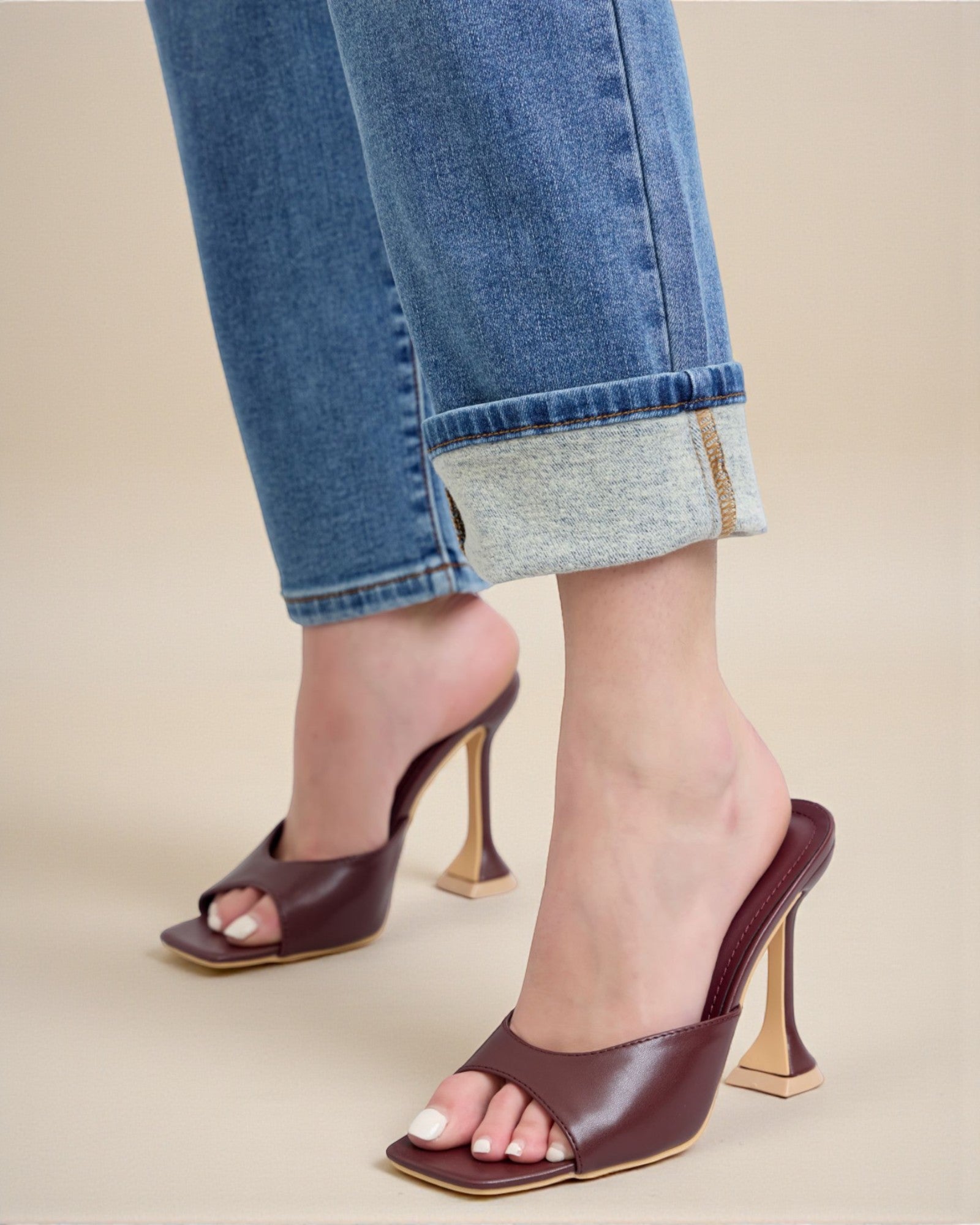 Brown high-heeled shoes worn with rolled-up jeans on a beige background