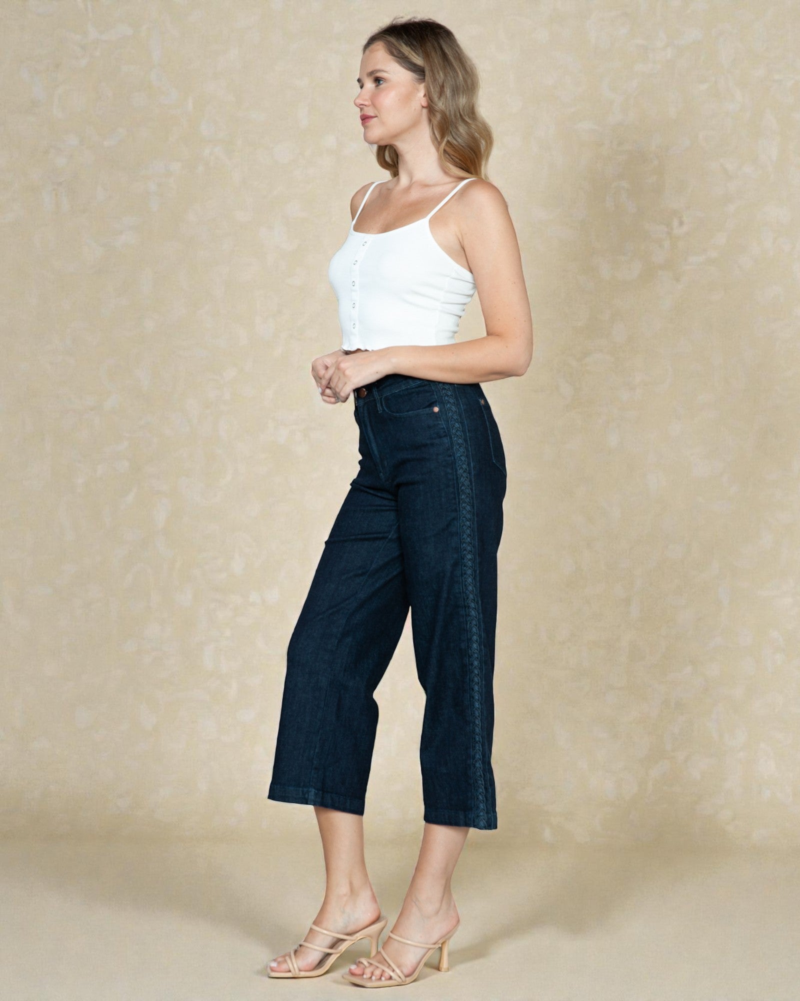 Woman wearing a white top and dark blue jeans against a beige background